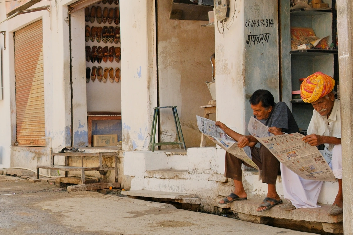 Scène de vie de village : la journée commence lentement, des hommes lisent le journal avant d’ouvrir leur atelier d’artisanat 