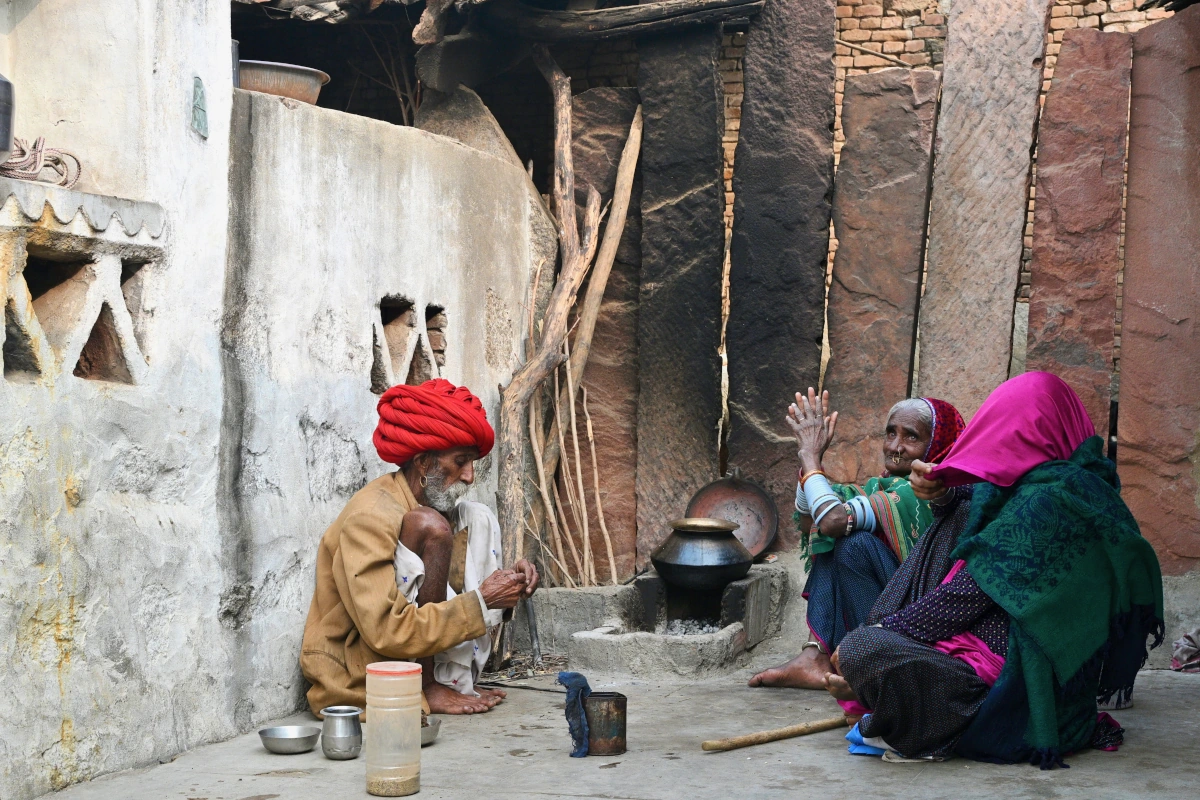 Artisan rajasthani assis paisiblement dans un village traditionnel, attendant que le chai mijote, entouré de ruelles étroites et de maisons en terre. 